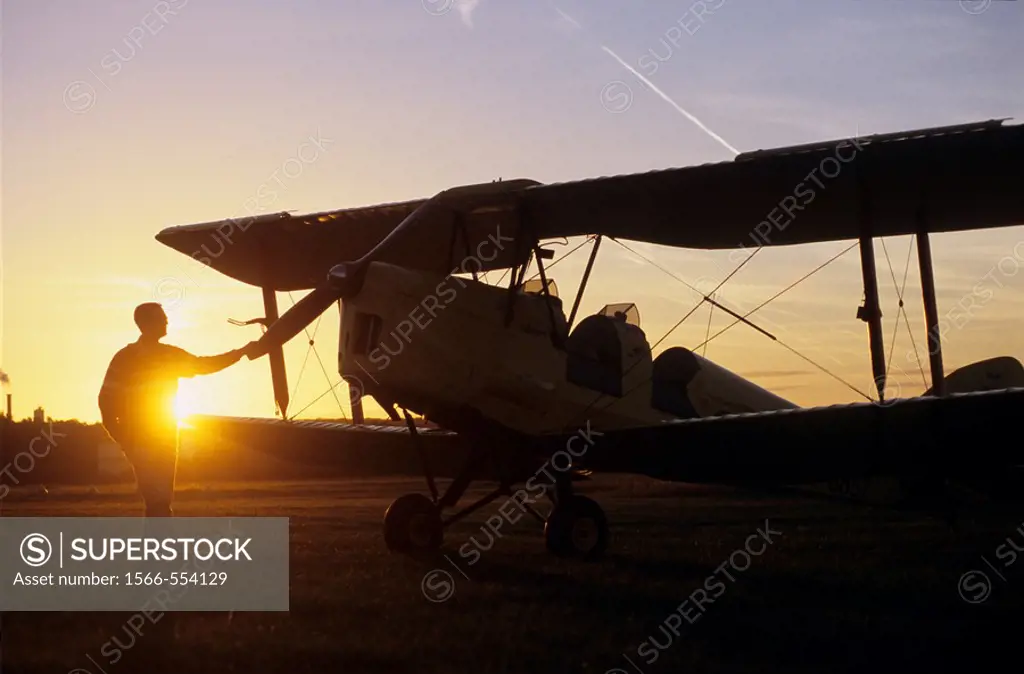 Pilot near an old trainer biplane De Havilland DH 82a Tiger Moth on sunset
