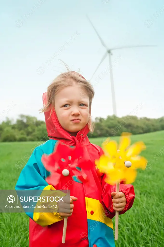 boy in colorful raincoat holding pinwheel standing in front of wind turbine