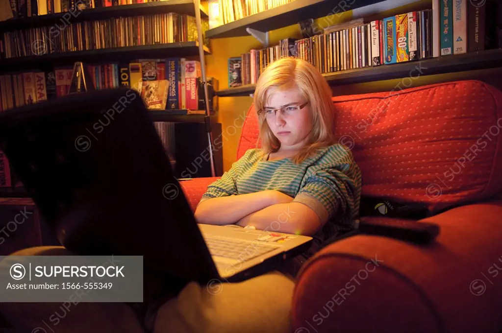 A fifteen year old teenage girl viewing her Facebook page on her laptop computer at home UK