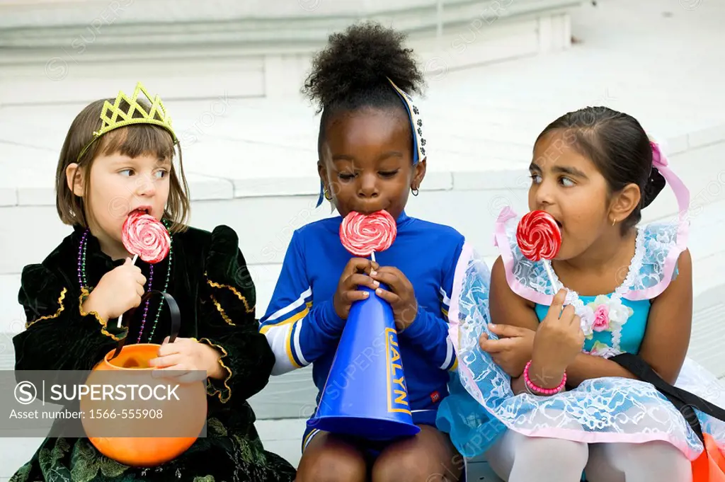 Little girls dressed in Halloween costumes enjoy their lollipops