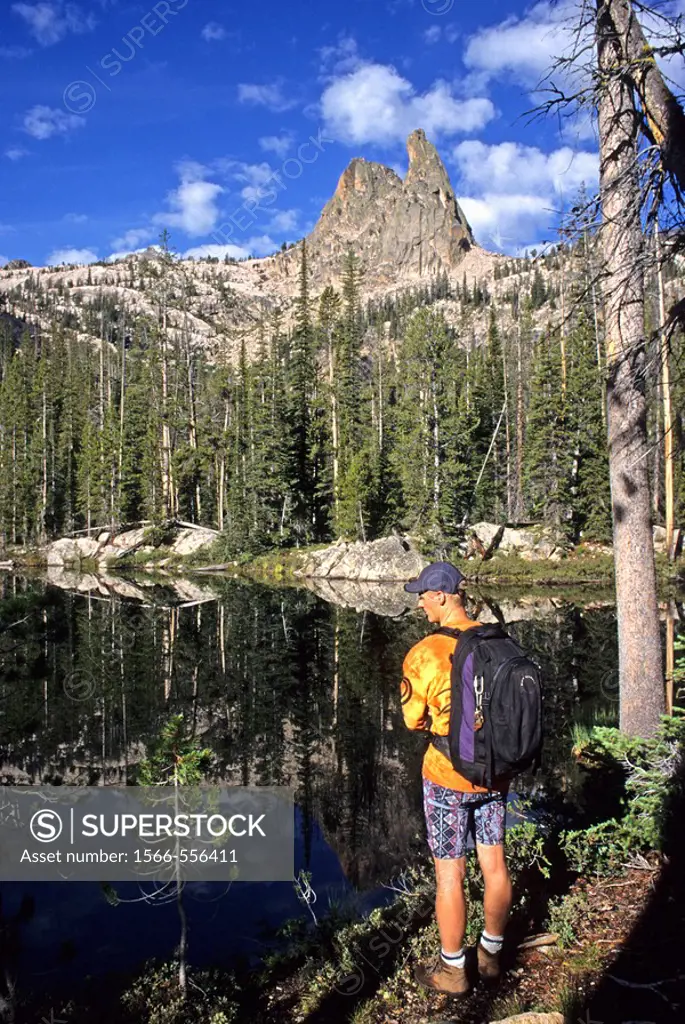 Man, pauses at a small lake while hiking to The Finger Of Fate for a rock climb of The Open Book route in the Sawtooth Mountains, Idaho