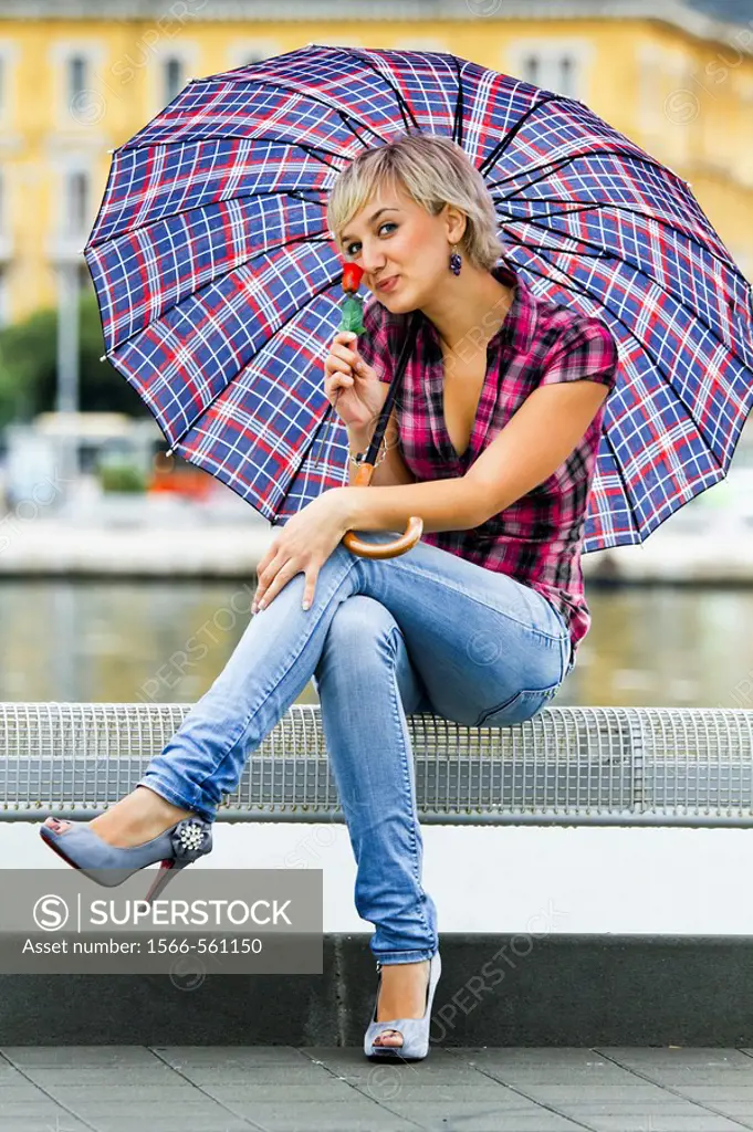 Sitting with a single rose in hand young woman is happy under an umbrella