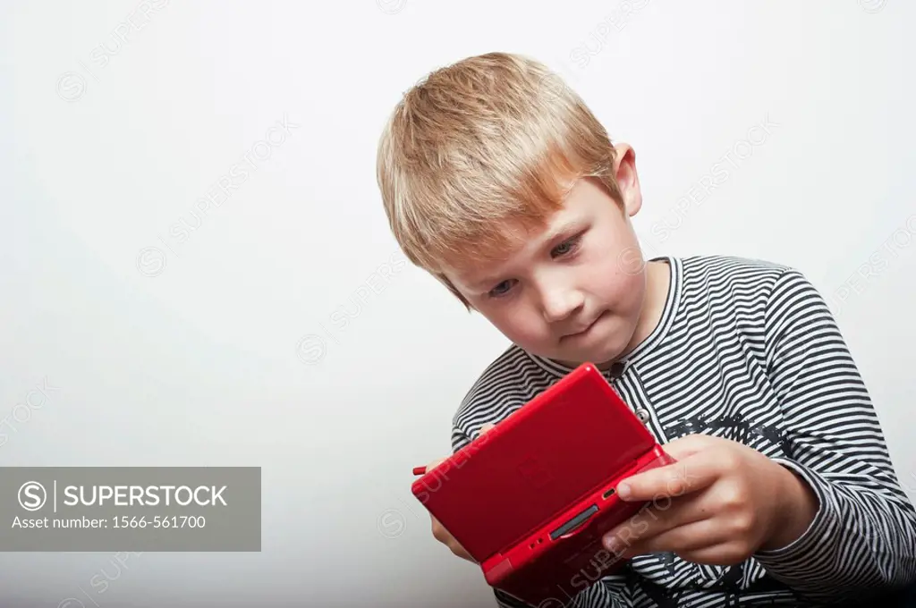 6 year old boy playing with a Nintendo DS handheld games console in the studio