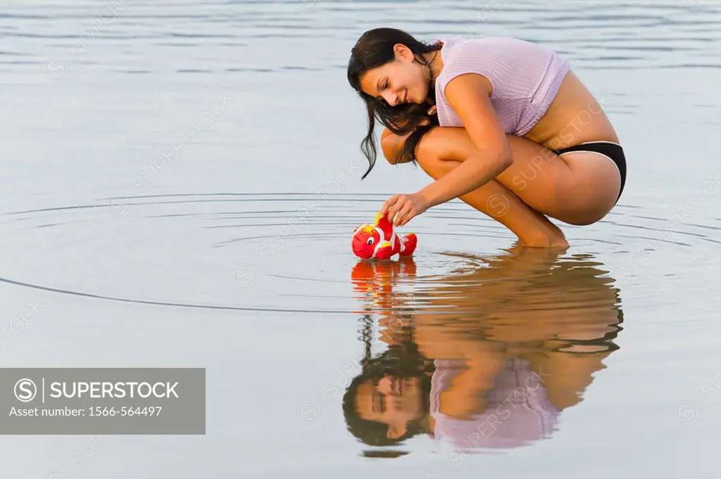 Young woman is placing a small toy fish on a water