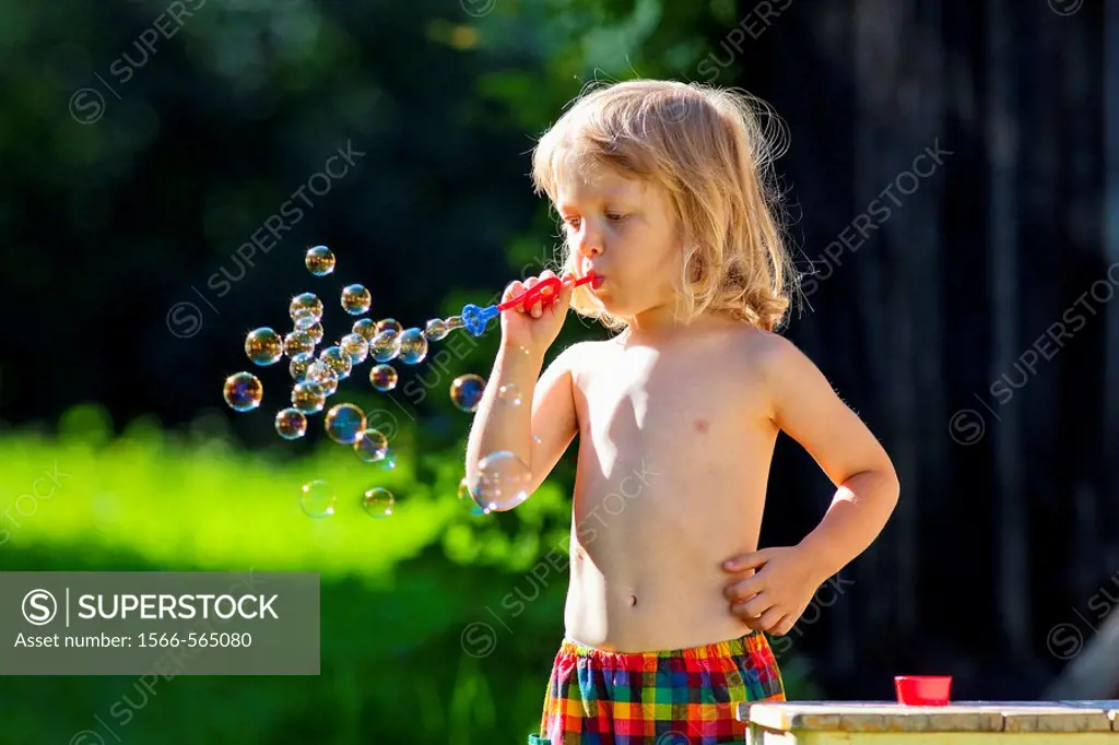 boy with long blond hair blowing soap bubbles