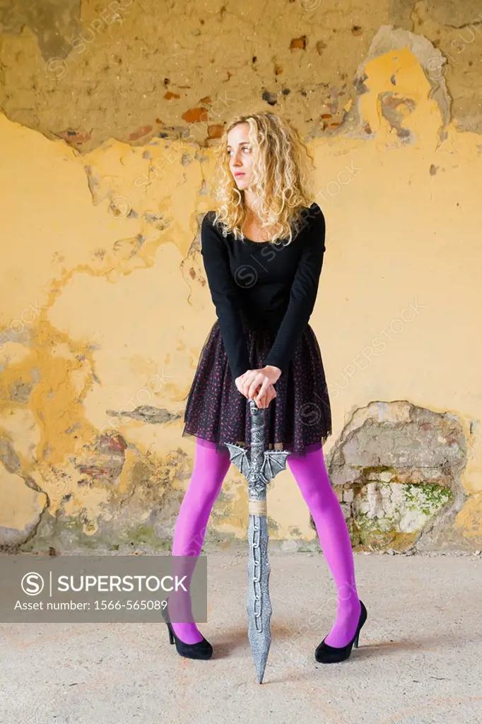 Standing with a fantasy sword between legs young woman