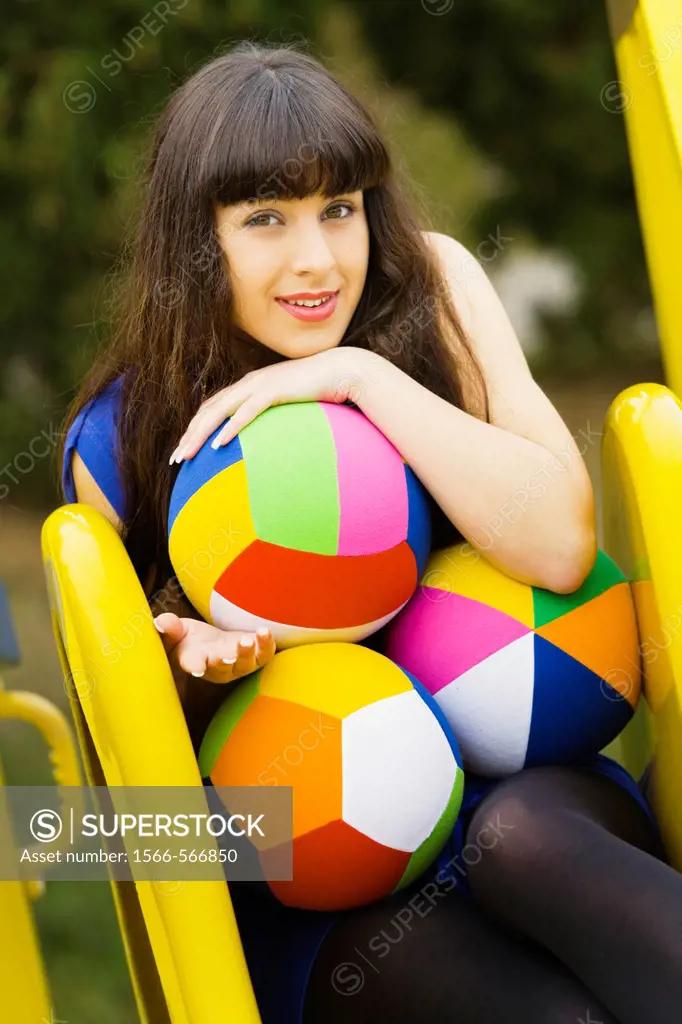 Playful on top of the slide young woman with colorful balls