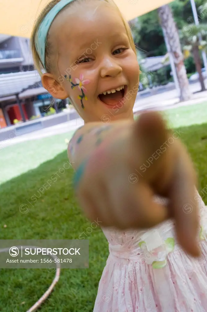 A happy 3 years old girl with face painting pointing to the camera
