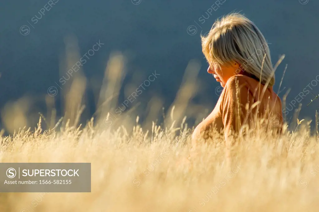 Blond female sitting in golden autumn grass in Arthur´s Pass, New Zealand