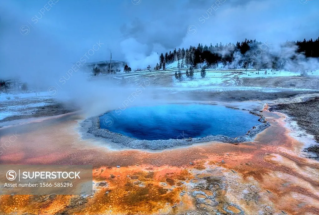 Crested Pool´s colors shine during the winter at Yellowstone National Park as Grand Geyser erupts in the background.