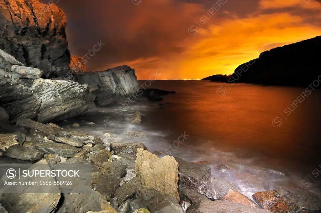 Night landscape of water and rocks photographed with long exposure time with a red sky orange background