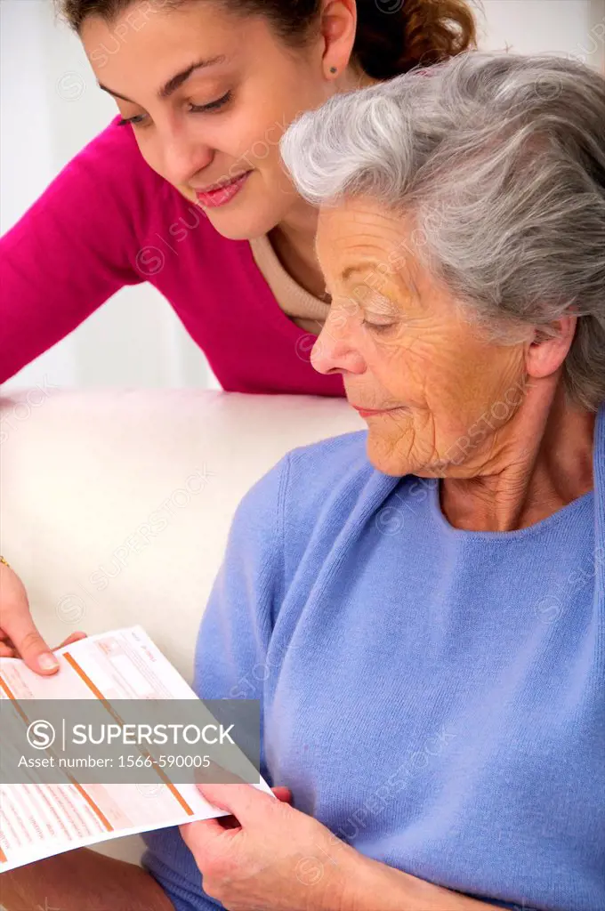 senior woman in a mauve cardigan, and young person who helps her reading medical papers at home