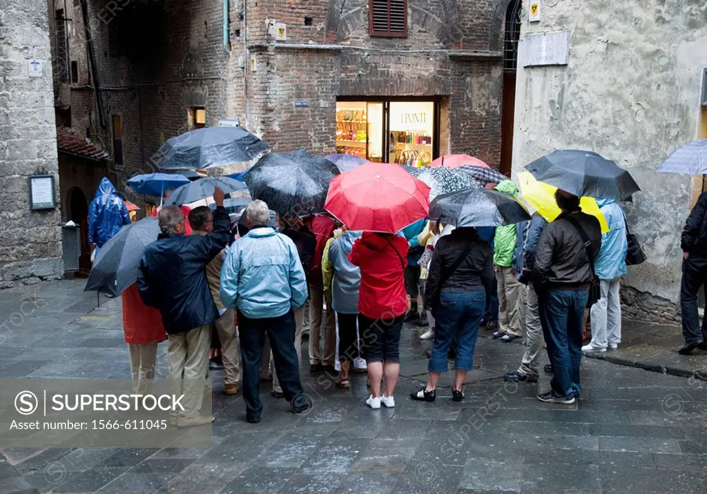 Italy, Tuscany, Siena. Group of tourists on tour of the old city on a rainy day, crowd together to hear tour guide.