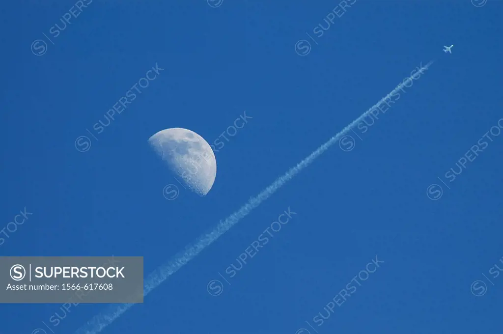 A passenger jet flies so high it appears to pass by the moon.