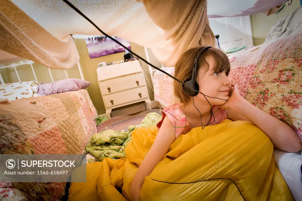 Preteen girl, with headphones, under a homemade bedroom tent