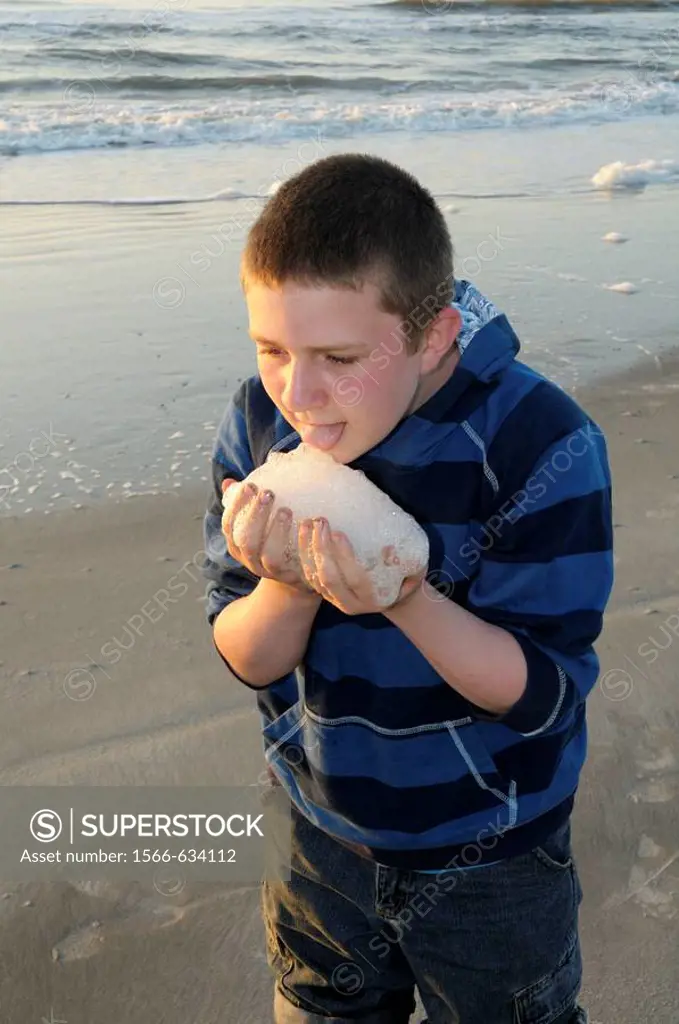Young boy tasting sea foam at sunrise on Hunting Island in South Carolina, USA  Hunting Island is well known for its five mile white sand beach and At...