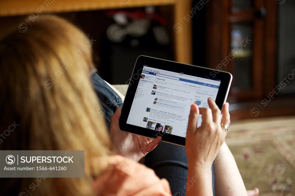 Close up of a woman hand holding an iPad checking her Facebook page