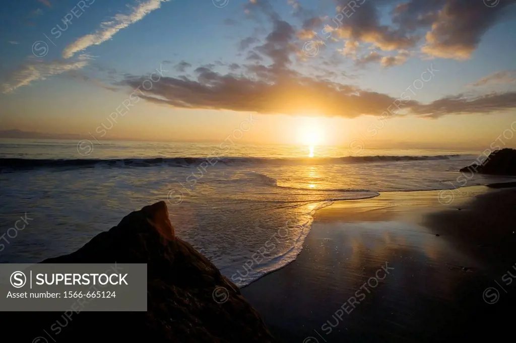 The sunset sets as clouds relect in the surf on a beach In Malibu, California, USA.