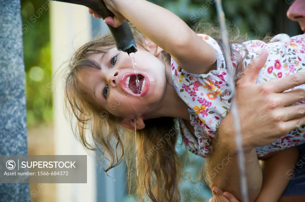 Girl being held while drinking water from a water fountain