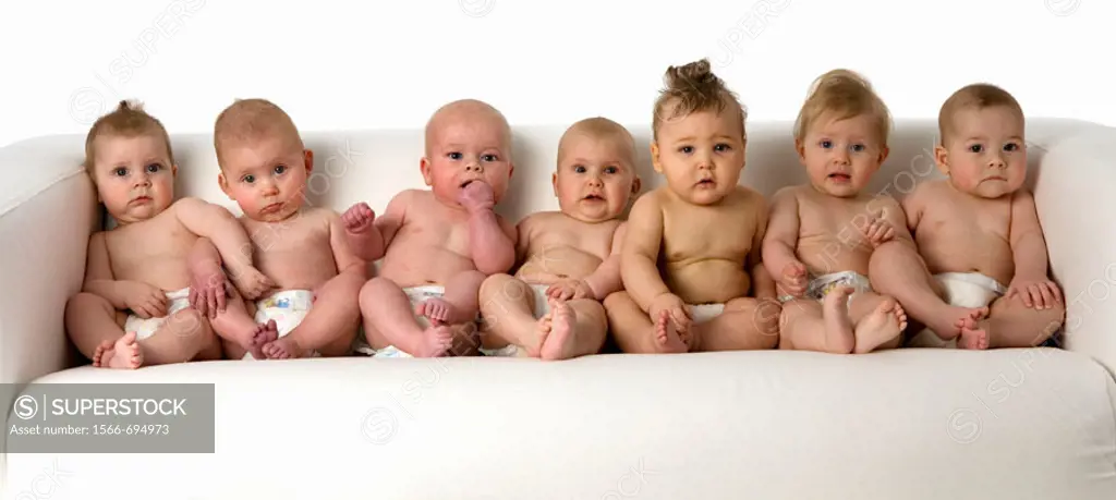 Seven babies sitting on a bench