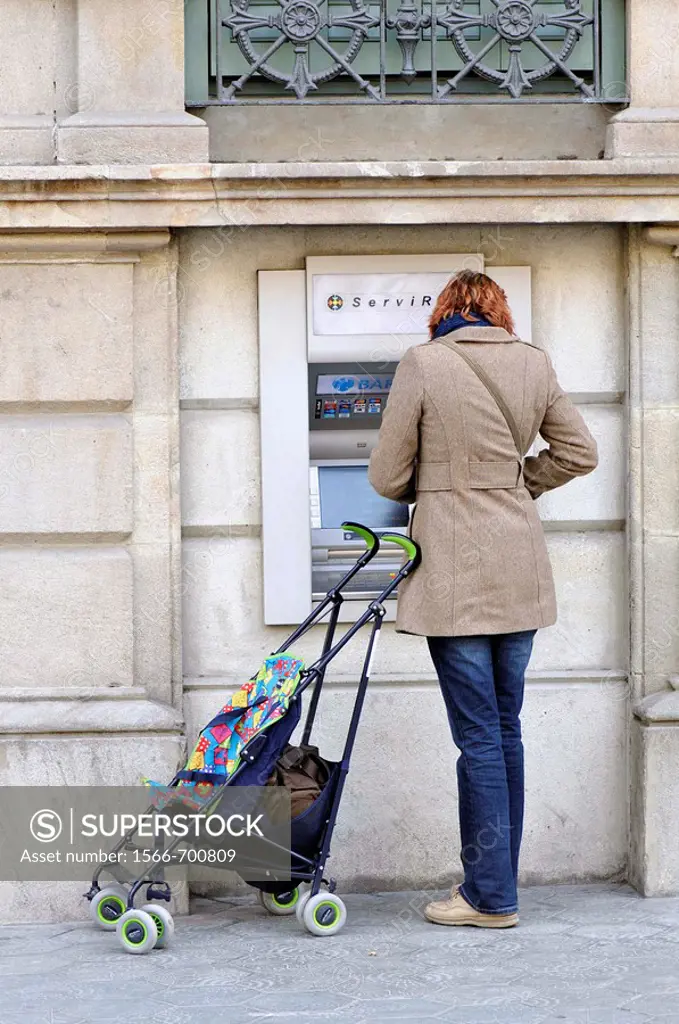 Girl with baby carriage using ATM, Barcelona, Catalonia, Spain
