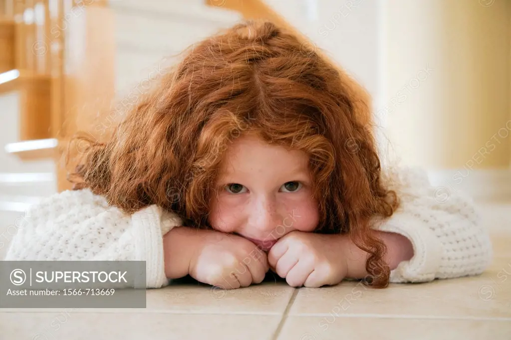 Portrait of five year old girl with red hair lying on tiles on floor