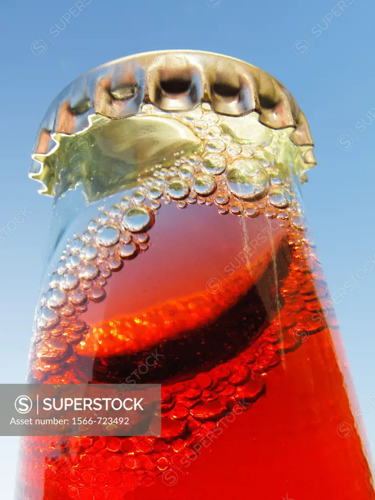 Shaken bottle neck with crown cap and a red liquid and many bubbles