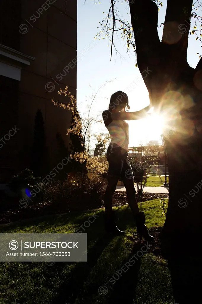 A young woman standing by a tree, backlit by the sun.