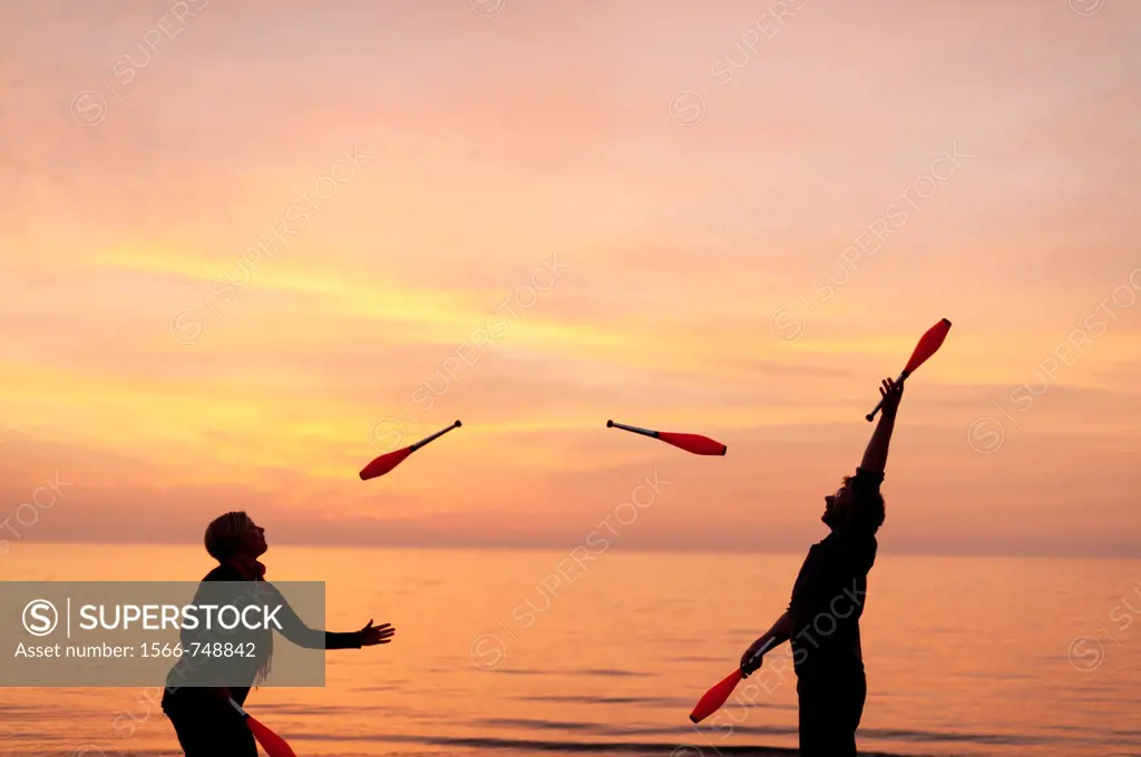 A young couple Juggling with clubs on the beach, spring evening sunset, Aberystwyth Wales UK