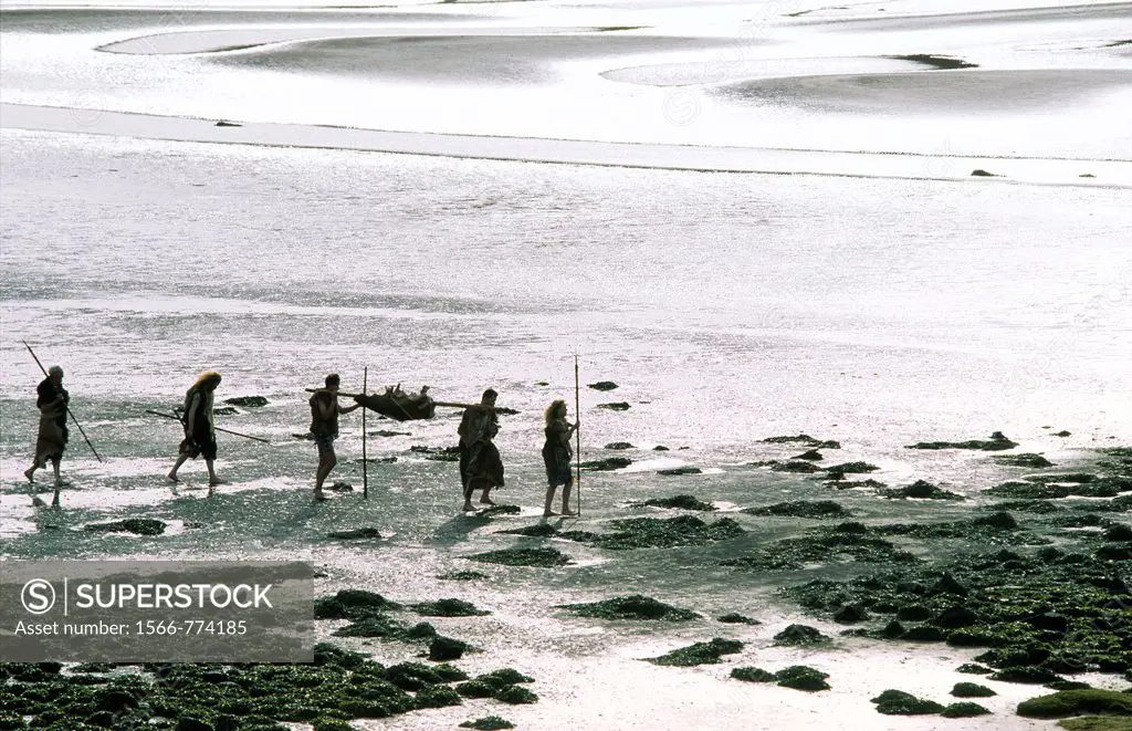 Neolithic prehistoric cave men walking on mud flat tidal estuary carrying deer food carcass and spears
