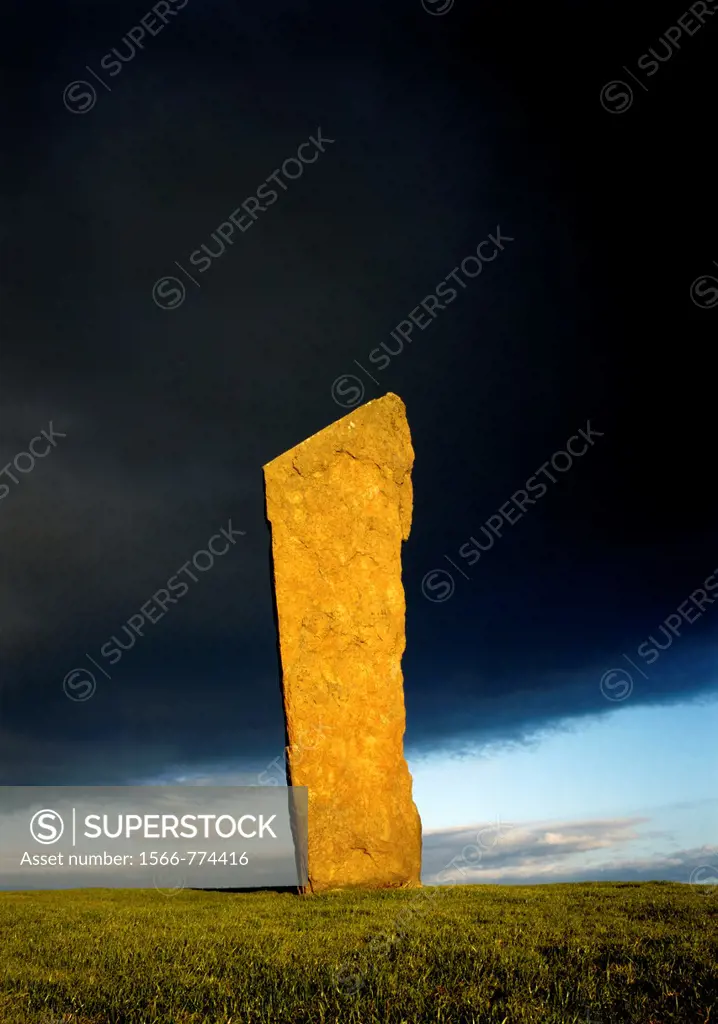 Stones of Stenness, Orkney, Scotland, UK  Tallest of the prehistoric stone circle stones lit by setting sun against rain cloud