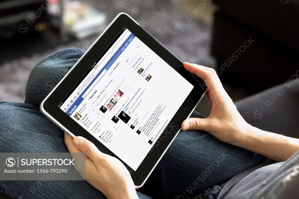Close up view of a woman handholding an ipad reading her Facebook newsfeed in a livingroom