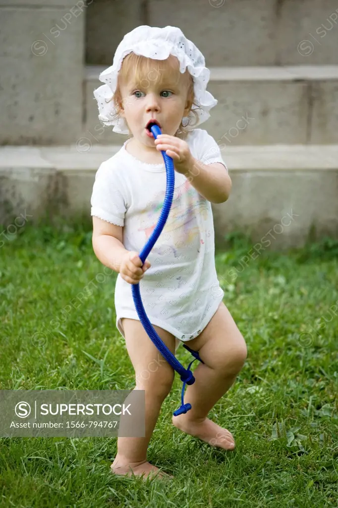 One Year Old Baby Girl Standing Outside and Blowing into Tube