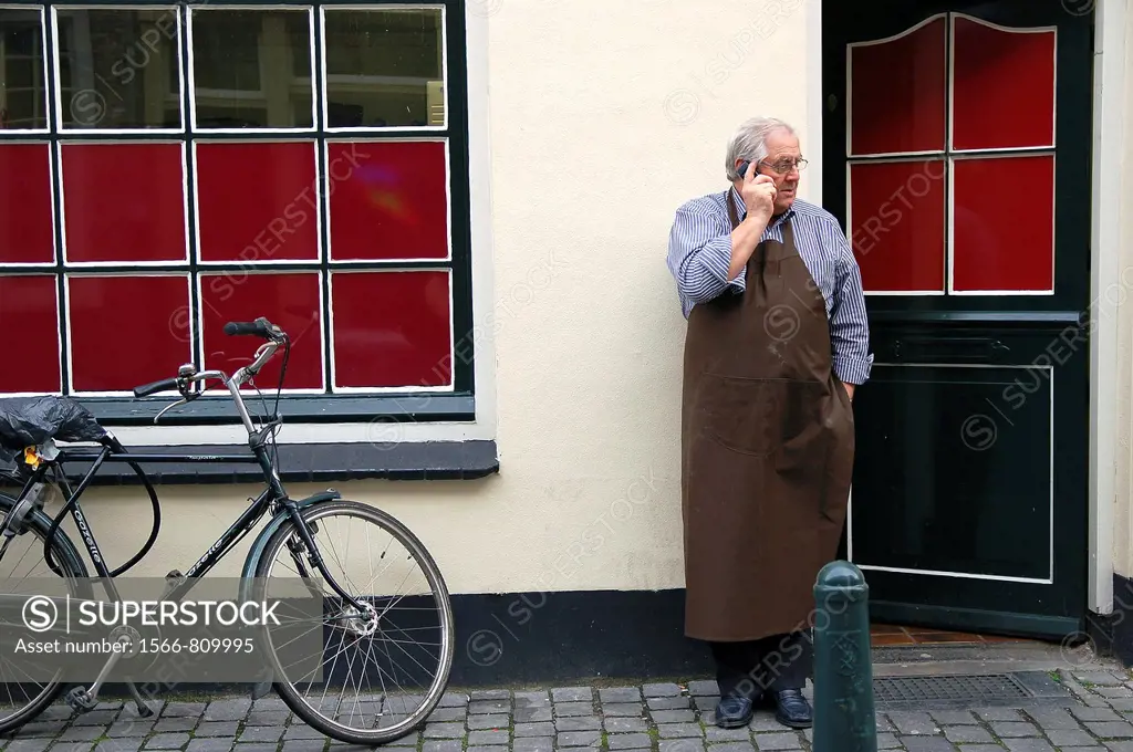 Man in apron making a phone call outside his shop.