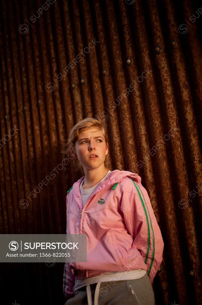 a 16 17 year old teenage girl standing alone against a rusty corrugated iron wall, uk