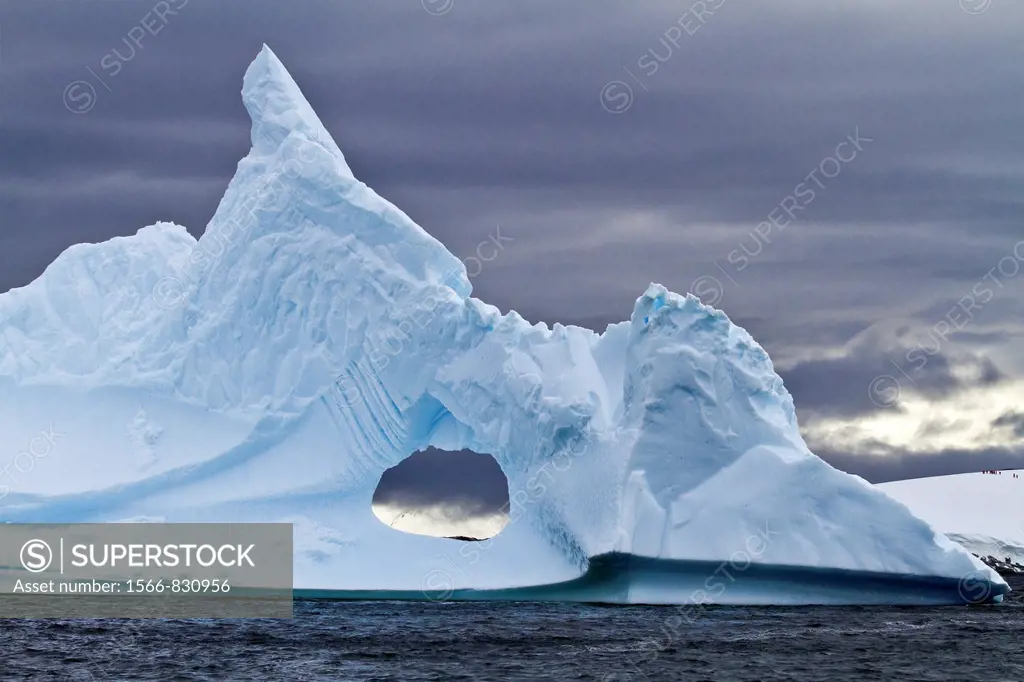 Unusual window formation in iceberg with Booth Island in the background on the western side of the Antarctic Peninsula during the summer months, South...