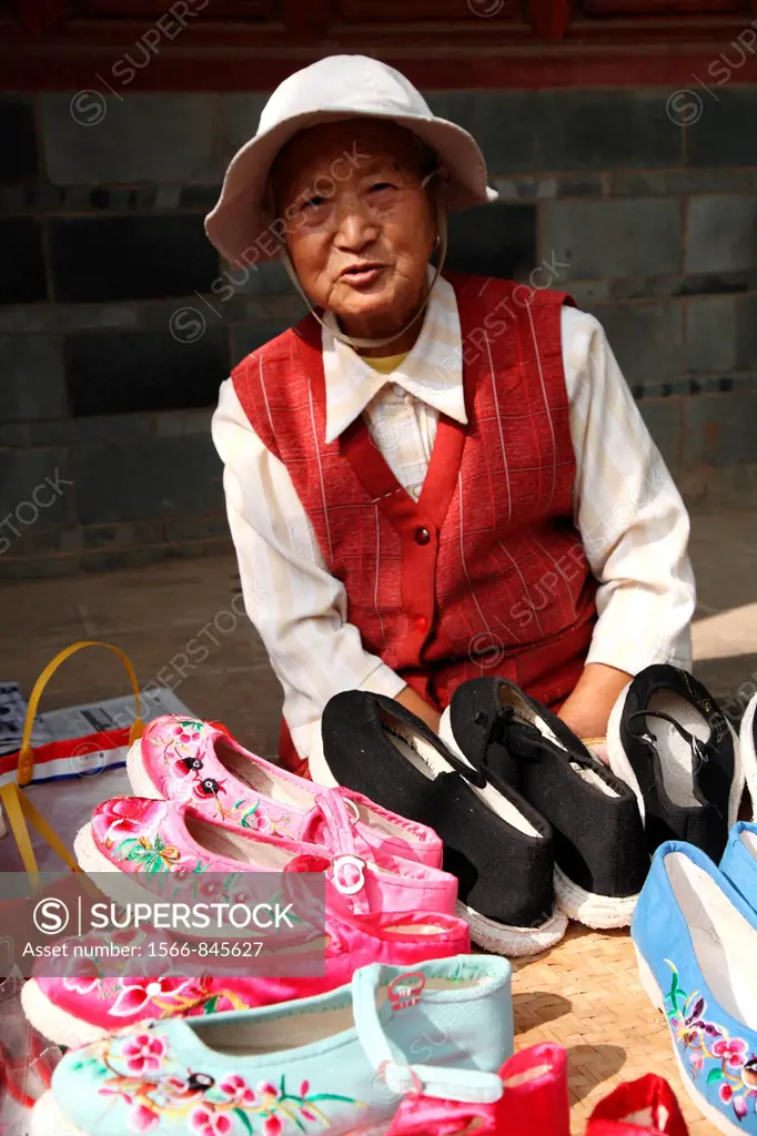 An old lady selling traditional style hand made embroidered shoes on old town street, Town of Guandu, Kunming, China