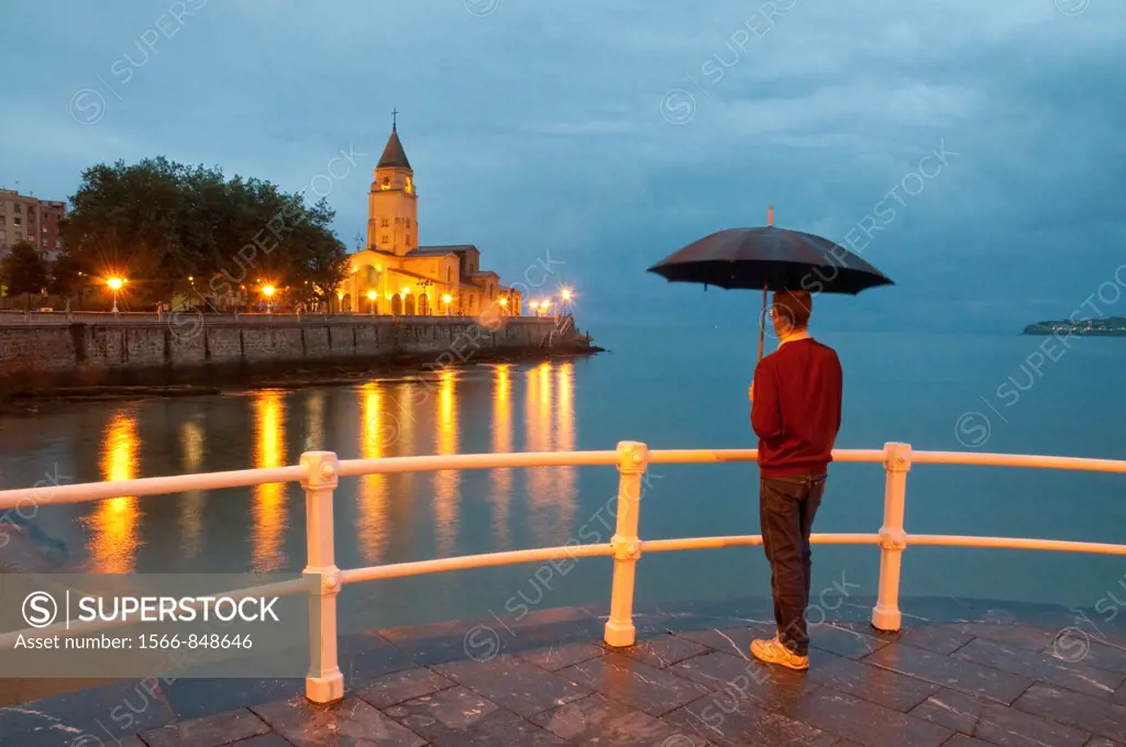 Man with umbrella on the promenade, night view. Gijón, Asturias province, Spain.