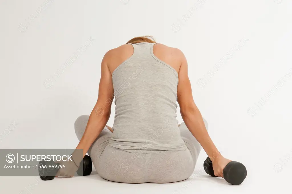 Young woman, redhead, sitting, exercising with weights at the gym