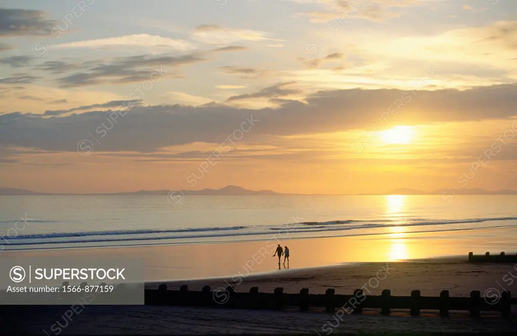 Sunset over the beach at the holiday seaside resort town of Barmouth in Gwynedd west Wales, UK  Young couple strolling on beach
