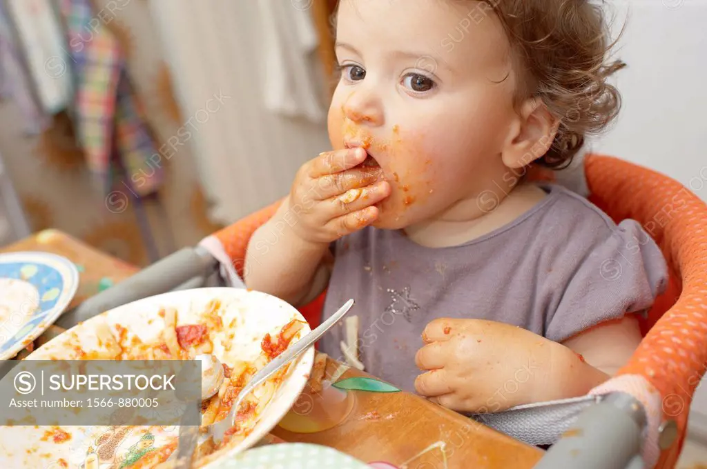 A seventeen months old baby girl eating tomato pasta using her hands