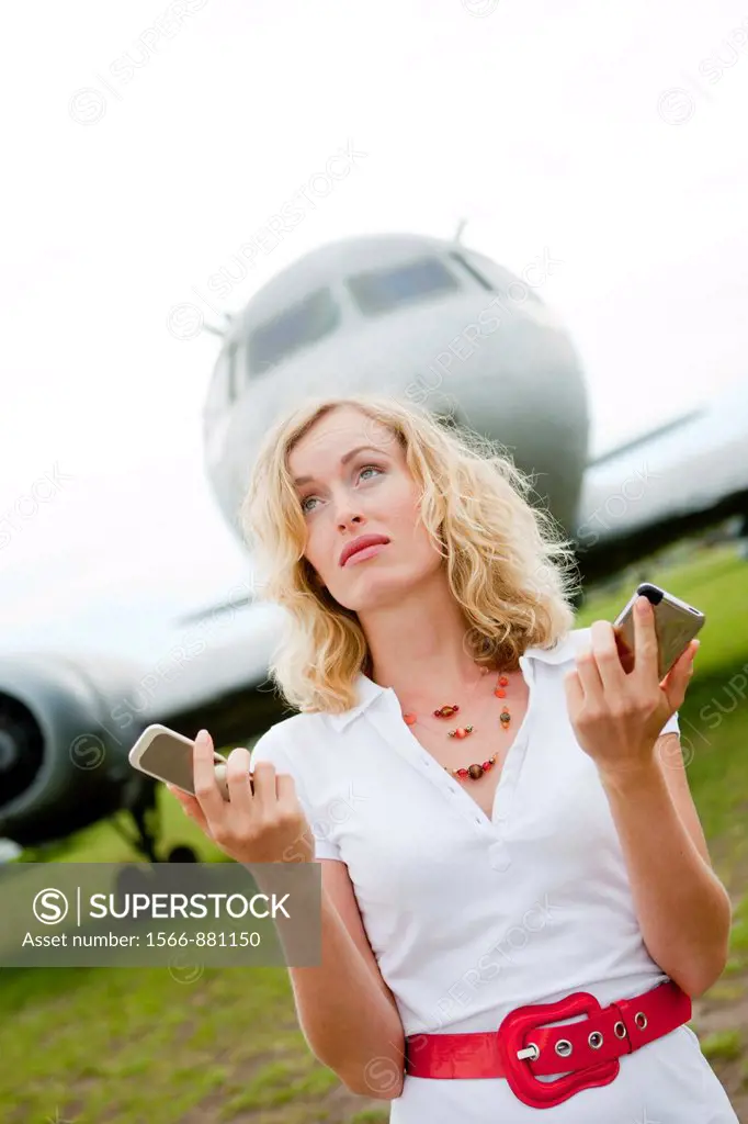 A business woman with two mobiles phones next to a plane
