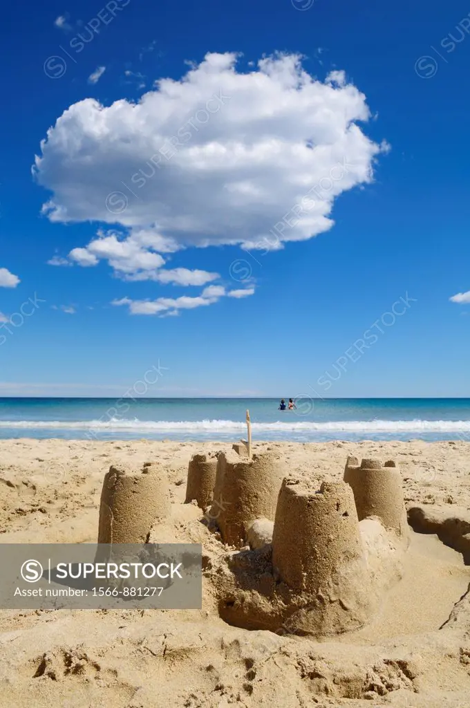 Sandcastles on a sandy beach on a perfect sunny summers day while children play in the sea