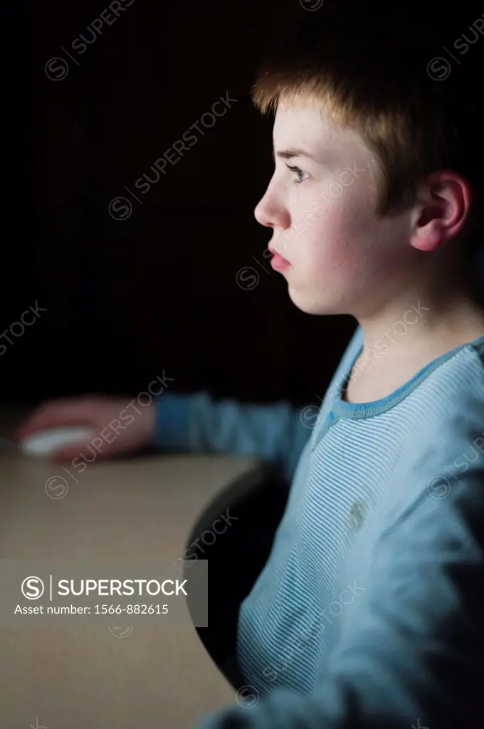 A 12 year old boy on his computer on Facebook internet website using very shallow depth of field