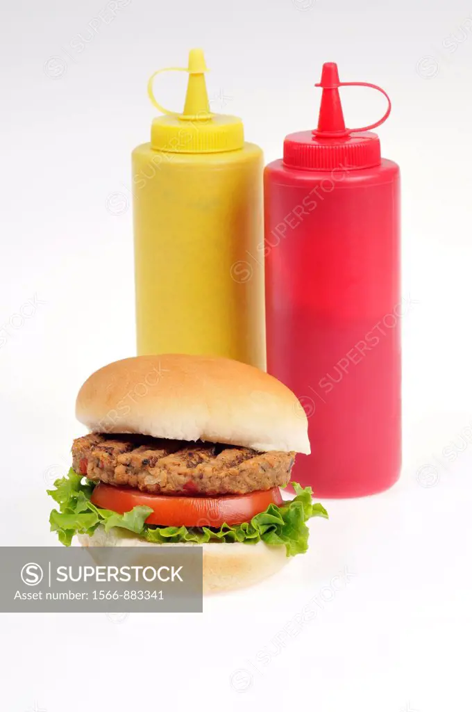 Grilled veggie burger with lettuce and tomato in bread roll with mustard & ketchup bottles on white background cutout