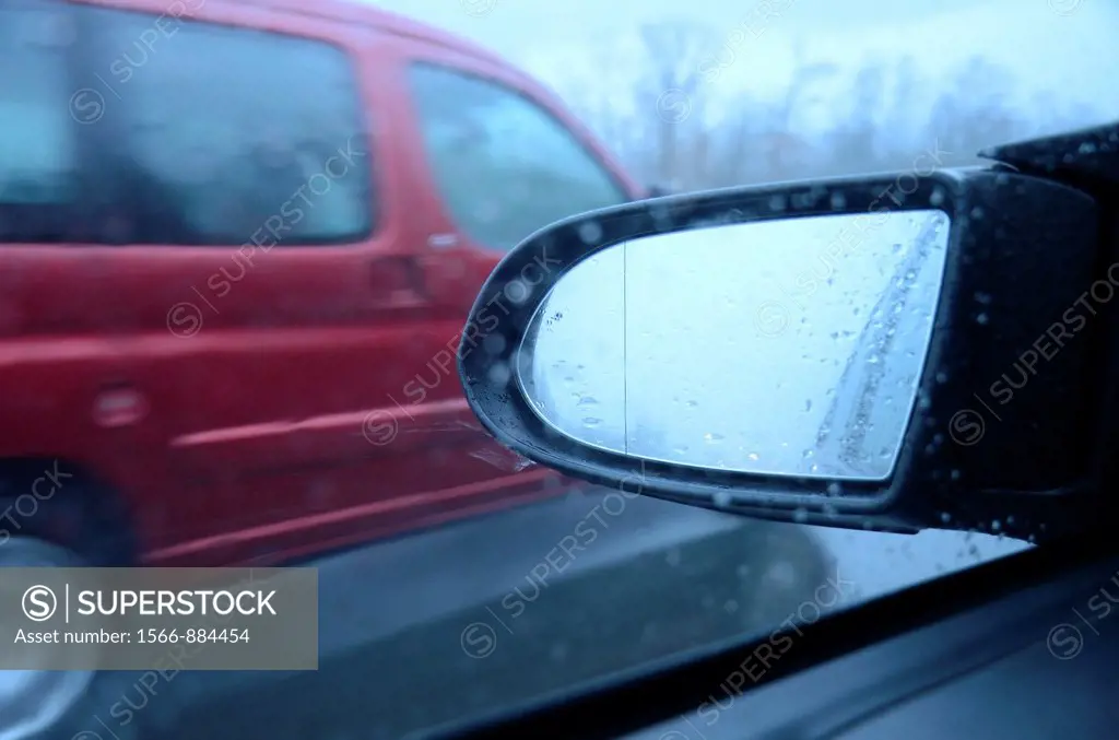 Side-view mirror and car passing on highway by rainy day, blurred motion