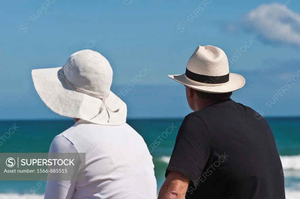 A man and woman sit and whatch the sea on a sunny afternoon  Hats protecting them from the hot summer sun  Muizenberg Beach, Cape Town, South Africa