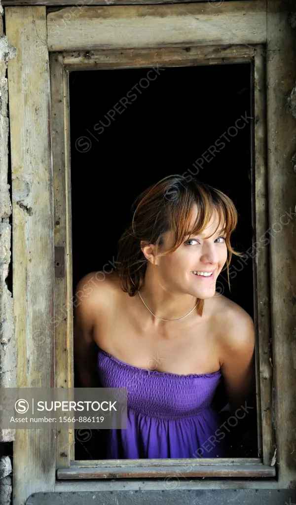 Portrait of a smiling young woman standing in window frame