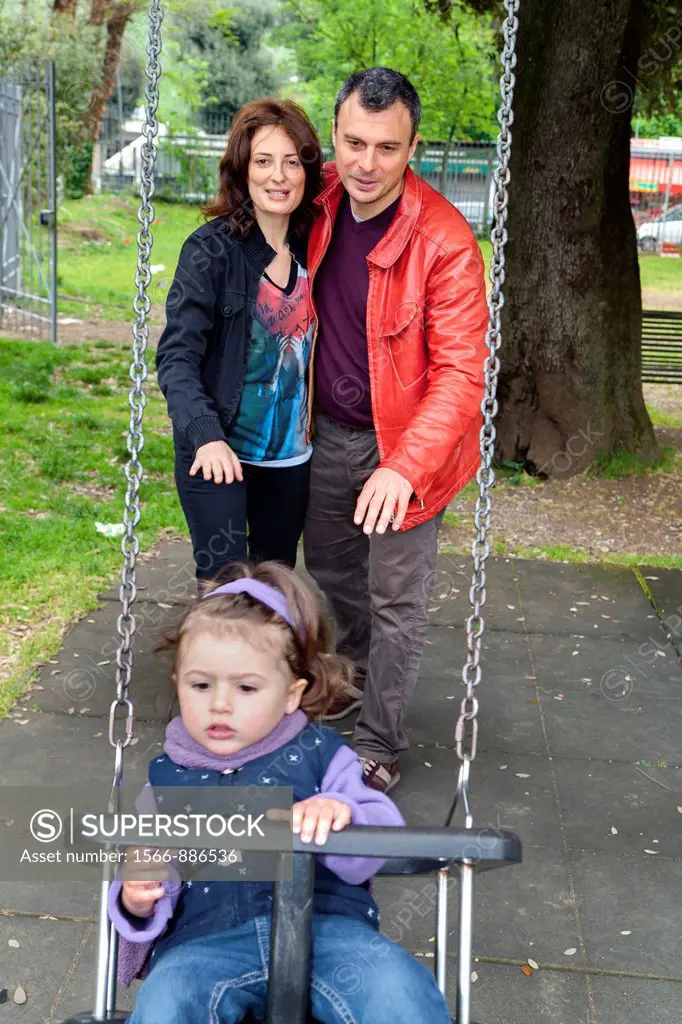 Father and mother pushing daughter on a swing