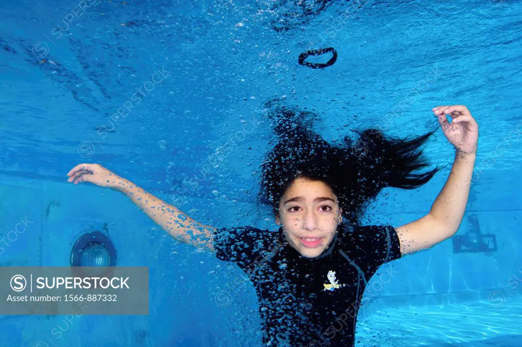 Young girl of 9 holds her breath while floating underwater in a swimming pool
